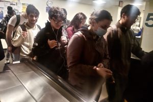 Students, some masked some not, approach an escalator