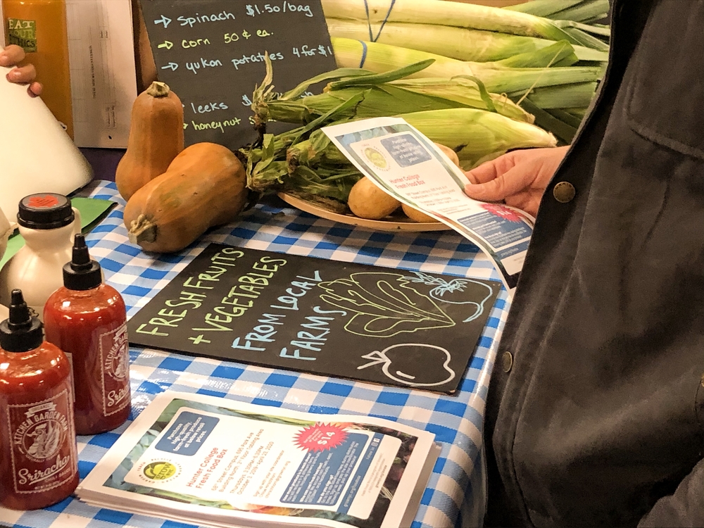 A man's hand holding a flyer next to the Fresh Food Box stand at Hunter North