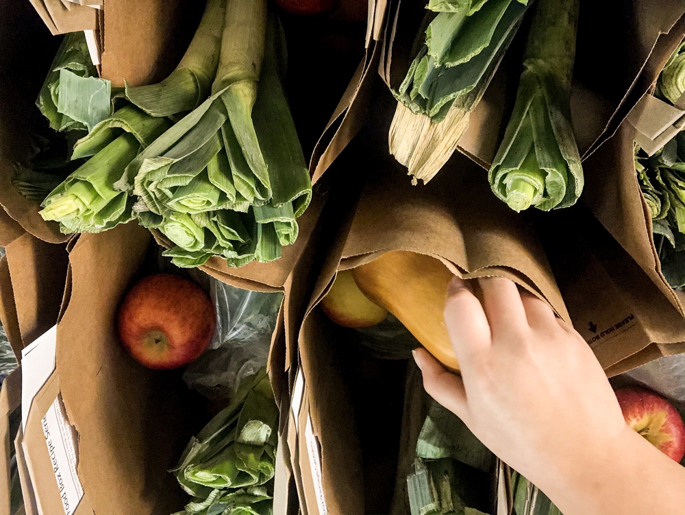 A hand sorts through the vegetables in a bag from the Fresh Food Box